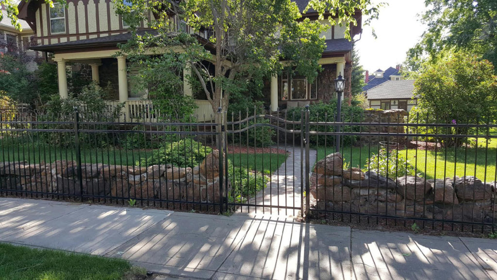 Beautiful backyard surrounded by custom black ornamental fence with an arched gate